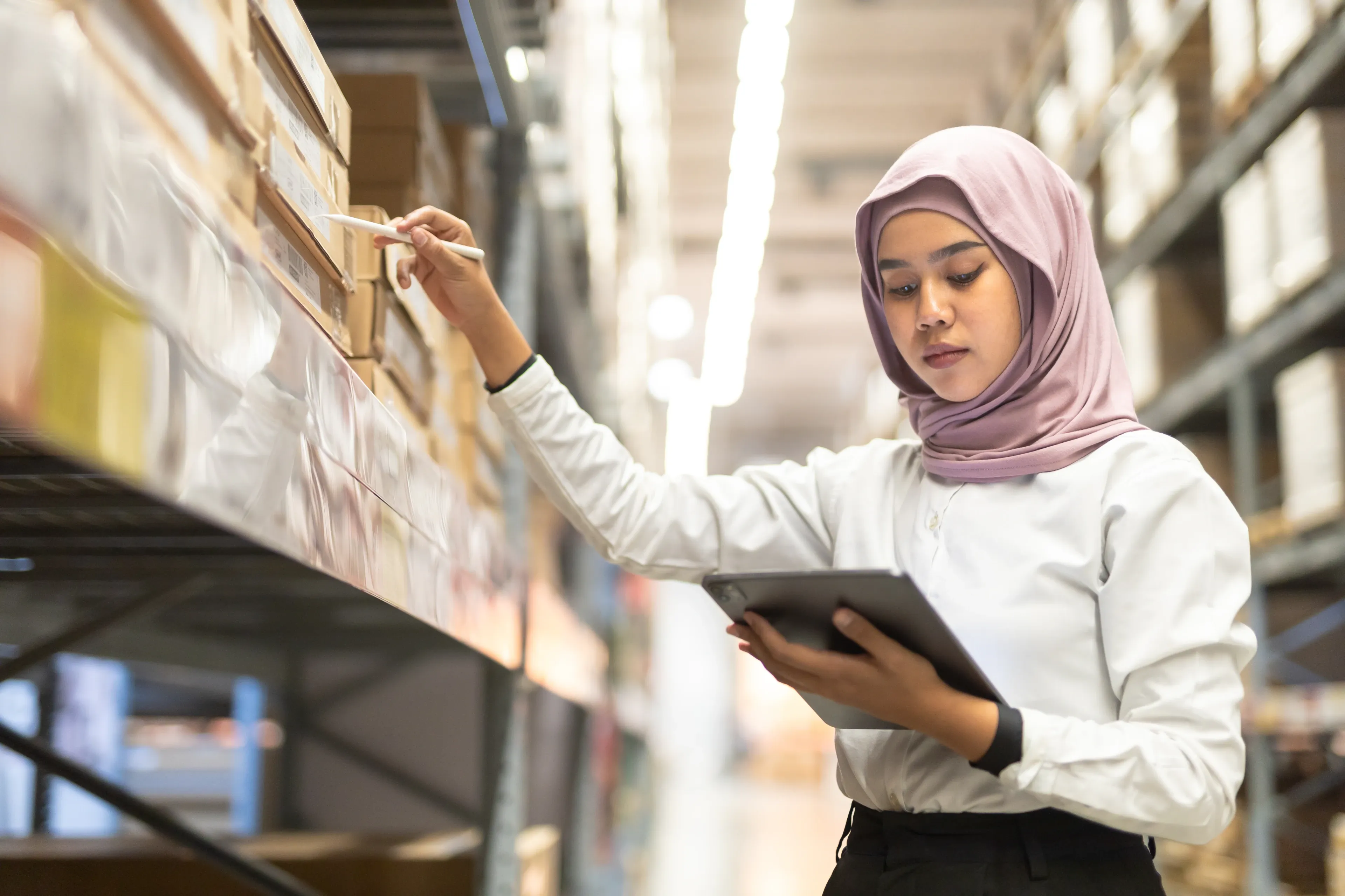 A Muslim woman using a tablet in a warehouse